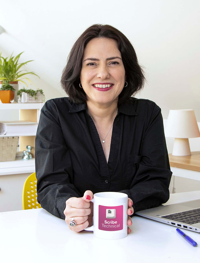 Lisa Orchard sitting behind a white desk holding a coffee cup with the words "Scribe Technical"